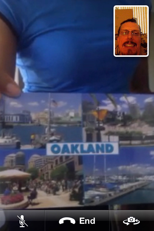 Venus holds up a postcard that shows tourist sites in Oakland, California. Steve's smile looks forced in the top right frame.